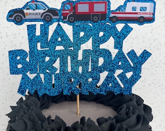 Könnte beinhalten: Blauer Glitzer-Kuchentopper mit den Worten "Happy Birthday" und einem Namen. Der Topper zeigt drei Spielzeugfahrzeuge: ein Polizeiauto, ein Feuerwehrauto und einen Krankenwagen.