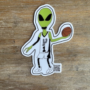 May include: A die-cut sticker featuring a green alien character wearing a white basketball jersey with the number 1 and a black star logo, holding a brown basketball. The character wears white sneakers and has a small QR code printed at the bottom right.