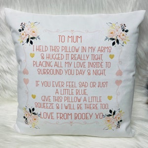 Peut inclure: Coussin carré blanc avec des motifs floraux et le texte "TO MUM" et un message d'amour. Le coussin a une bordure décorative avec des cœurs et des fleurs. Le texte est de couleur rose tendre.
