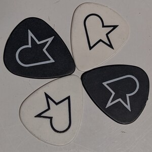 May include: Four guitar picks with black and white designs. Each pick features a different abstract shape with a star-like point.