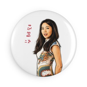 May include: A round button featuring an illustration of a person with long dark hair wearing a white sleeveless dress with a colorful dragon design. The image includes vertical red text on the left side against a plain white background.