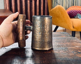 May include: A rustic, hammered metal mug with a wooden handle. The handle has a metal plate with the words "NEVER LOOK BACK" engraved on it.