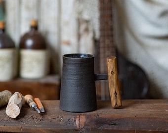 Dark rustic handmade ceramic mug with juniper wood handle. Charcoal gray and bronze tall mug made of black clay. Wooden handled mug.