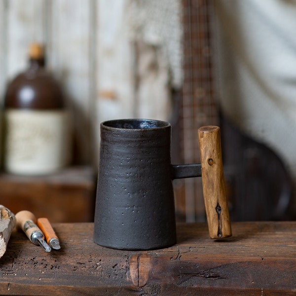 Dark rustic handmade ceramic mug with juniper wood handle. Charcoal gray and bronze tall mug made of black clay. Wooden handled mug.