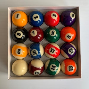 May include: A set of 15 billiard balls in a white box. The balls are numbered 1 through 15 and are arranged in a grid pattern. The balls are various colors, including red, yellow, blue, green, and black.