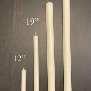 May include: Four off-white taper candles arranged vertically by height. The candles are labeled with their respective lengths of 12 inches, 19 inches, 26 inches, and 34 inches. Each candle features a simple cylindrical shape with a small wick at the top.