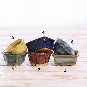 May include: A collection of six small ceramic bonsai pots in various shapes and colors, including green, yellow, dark blue, reddish-brown, and grey-blue glazes. Each pot is numbered from one to six, featuring distinct rim and base designs.