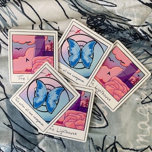 May include: A collection of rectangular stickers featuring illustrations. Some stickers depict a lighthouse scene with pink and purple hues, while others showcase a blue butterfly. Text includes "The Lighthouse" and "This action will have consequences..."