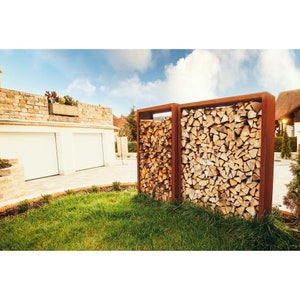 Peut inclure: Deux supports en métal rouillé pour le stockage de bois, remplis de bois de chauffage empilé. Les supports sont dans une cour herbeuse devant une maison avec une porte de garage blanche.