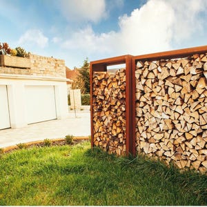 Może przedstawiać: Jednostka do przechowywania drewna opałowego ze stali odpornej na warunki atmosferyczne, wypełniona starannie ułożonymi kłodami. Jednostka znajduje się w trawiastym ogrodzie z domem i garażem w tle, pod częściowo zachmurzonym niebem.