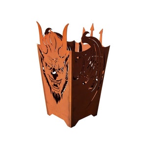 Puede incluir: Un hogar de fuego de metal oxidado con forma de cabeza de demonio con alas. El hogar tiene un diseño recortado de una cara de demonio con cuernos y una expresión de gruñido. Las alas también están recortadas y tienen un diseño detallado.