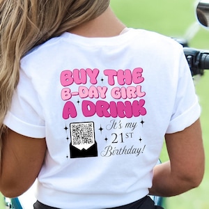 May include: White t-shirt with pink text that reads "BUY THE B-DAY GIRL A DRINK It's my 21ST Birthday!" with a QR code and pink stars. The person wearing the shirt is sitting on a motorcycle.