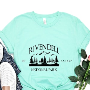 May include: A turquoise t-shirt with a black graphic design that says "Rivendell National Park Est. S.A. 1697". The graphic features a mountain range with trees.