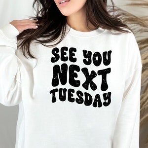 May include: White sweatshirt with black text that reads "See you next Tuesday" in a retro font.