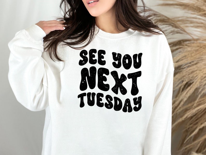 May include: White sweatshirt with black text that reads "See you next Tuesday" in a retro font.