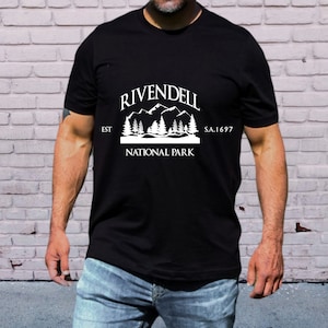 May include: Black t-shirt with a white graphic of a mountain range and trees. The graphic says "Rivendell National Park" with "Est" and "S.A. 1697" on either side.