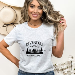 May include: Gray t-shirt with a black graphic of a mountain range and trees. The graphic says "Rivendell National Park Est S.A. 1697"