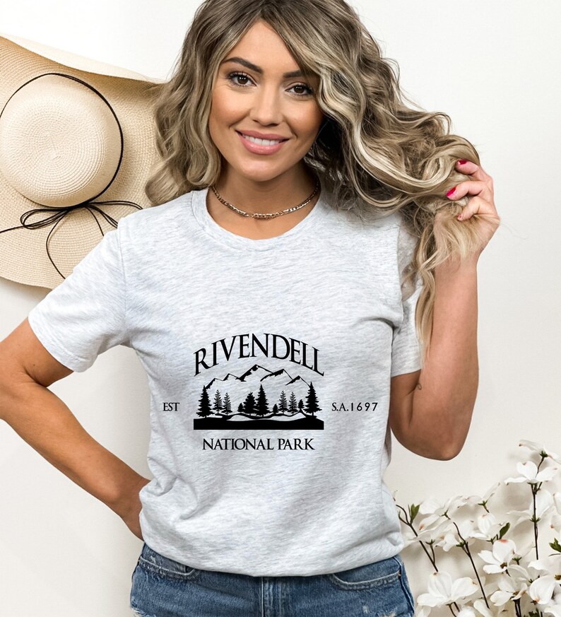 May include: Gray t-shirt with a black graphic of a mountain range and trees. The graphic says "Rivendell National Park Est S.A. 1697"