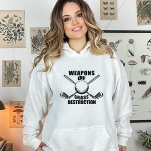 May include: White hooded sweatshirt with black text and graphic that reads "Weapons of Grass Destruction" with a golf club and golf ball.