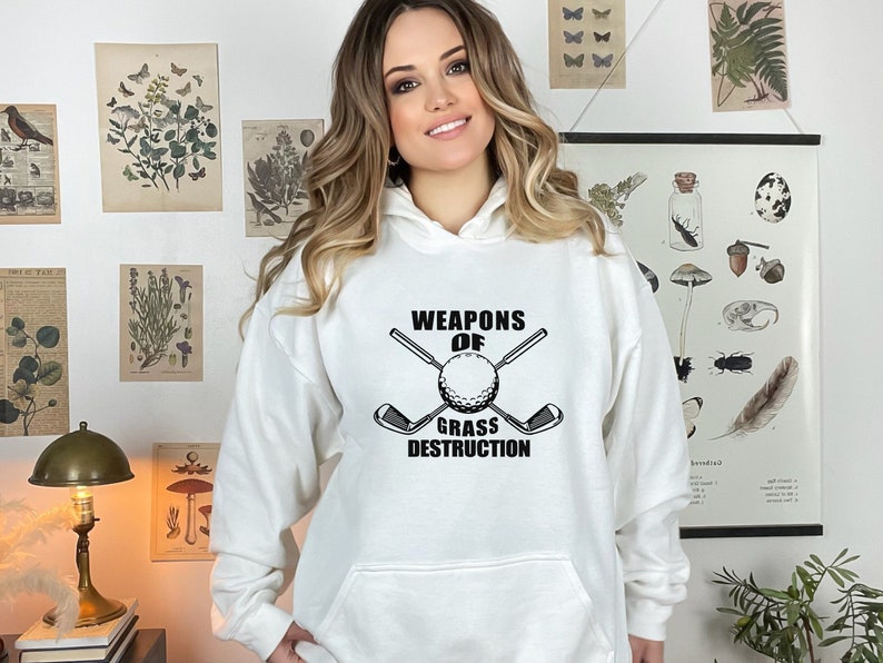 May include: White hooded sweatshirt with black text and graphic that reads "Weapons of Grass Destruction" with a golf club and golf ball.