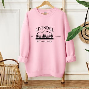 May include: Pink sweatshirt with a black graphic print of a mountain range and the text "Rivendell National Park Est. S.A. 1697".