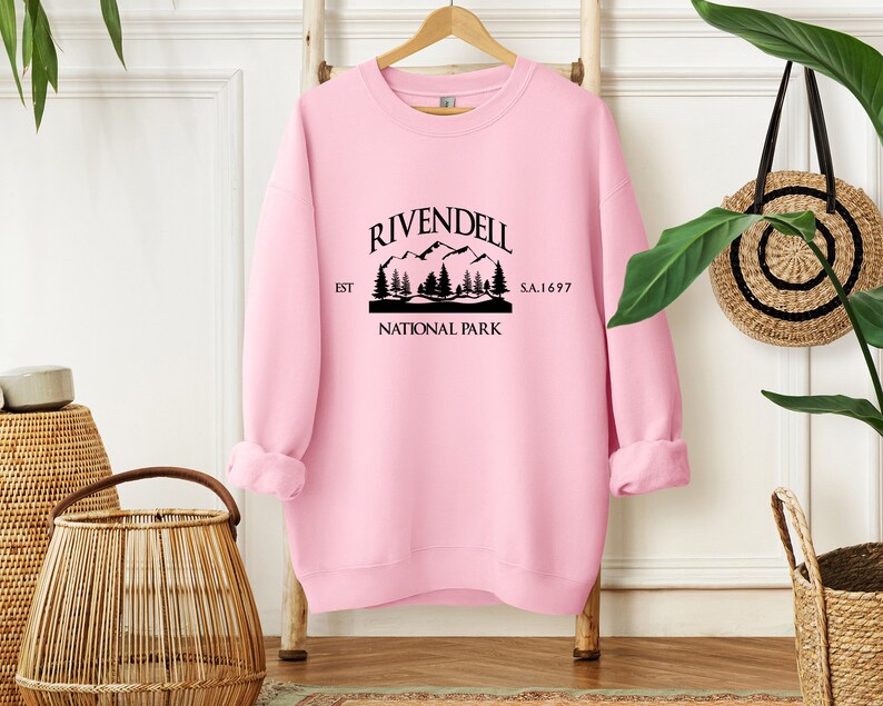 May include: Pink sweatshirt with a black graphic print of a mountain range and the text "Rivendell National Park Est. S.A. 1697".