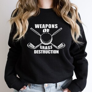 May include: Black sweatshirt with white text that reads "Weapons of Grass Destruction" and a graphic of a golf ball with two crossed golf clubs.