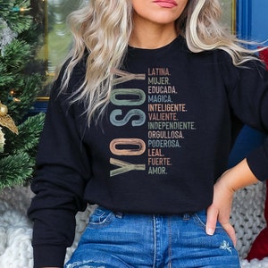 May include: Black sweatshirt with a vertical graphic design in rainbow colors. The graphic says "YO SOY" and lists a series of Spanish words describing a woman's qualities.
