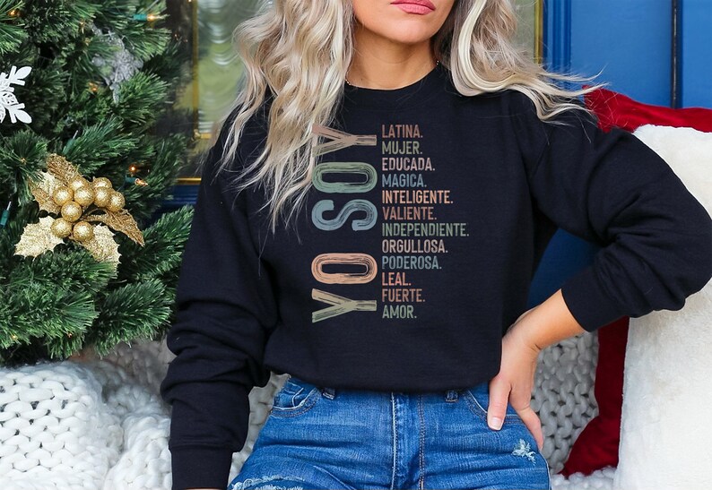 May include: Black sweatshirt with a vertical graphic design in rainbow colors. The graphic says "YO SOY" and lists a series of Spanish words describing a woman's qualities.