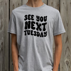May include: A heather grey t-shirt with the text "See You Next Tuesday" in black, retro-style lettering.