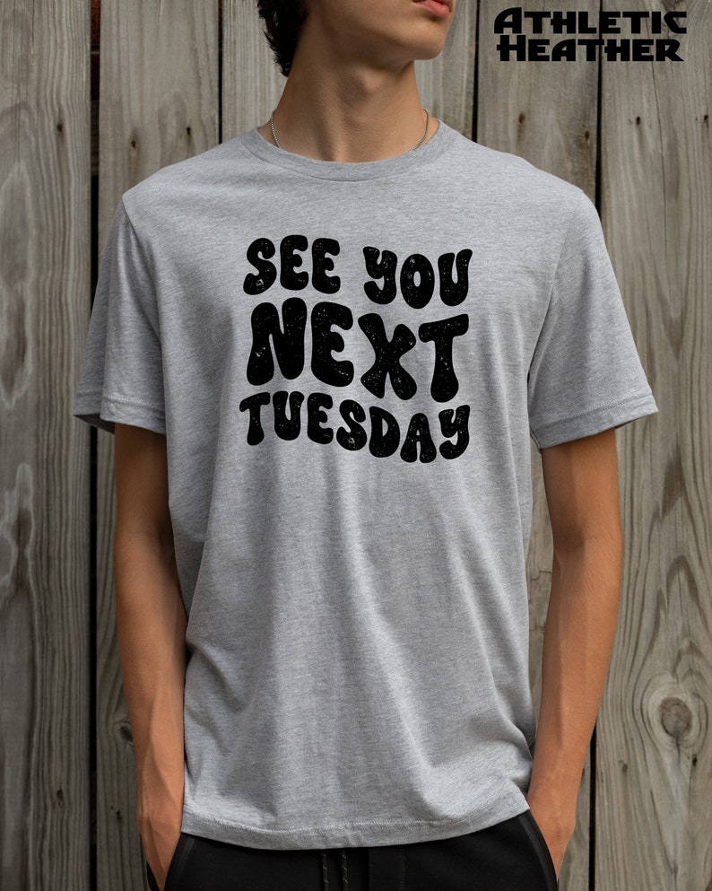 May include: A heather grey t-shirt with the text "See You Next Tuesday" in black, retro-style lettering.