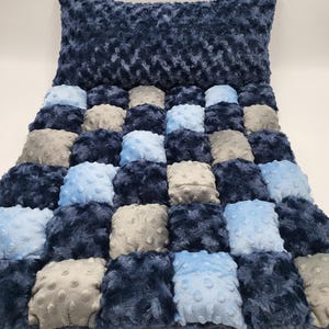 May include: A rectangular pillow and a matching quilt featuring a patchwork design of plush, textured squares in shades of navy blue, light blue, and grey. Each square has a raised, dimpled surface pattern, creating a soft, tactile appearance.
