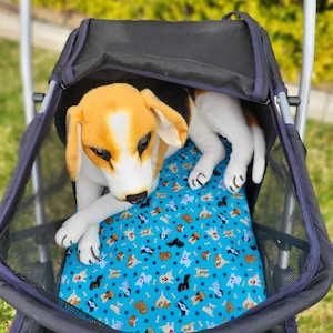 May include: A plush beagle dog toy rests in a black and navy blue pet stroller. The dog has brown, black, and white fur. The stroller has a blue patterned cushion with dog illustrations.