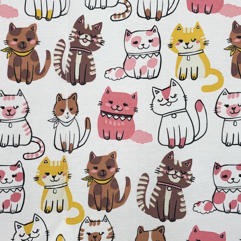 May include: A white fabric featuring a repeating pattern of cartoon cats in various colors including brown, pink, yellow, and white. The cats are depicted in different poses, some wearing collars or small neckerchiefs, with simple line-drawn facial features.