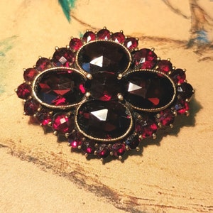 May include: A vintage brooch with a cluster of five red garnet stones surrounded by smaller red garnet stones in a gold setting.