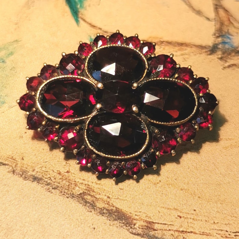 May include: A vintage brooch with a cluster of five red garnet stones surrounded by smaller red garnet stones in a gold setting.