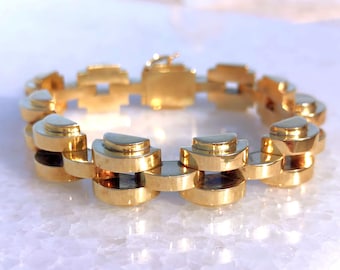 May include: A gold bracelet with a geometric design. The bracelet is made of interlocking links that are shaped like half-circles.