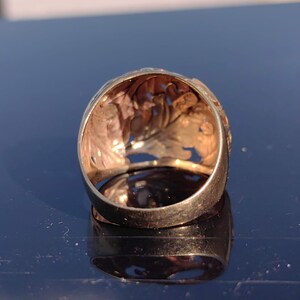 May include: A gold ring with a detailed, intricate design. The ring is made of yellow gold and has a filigree pattern.