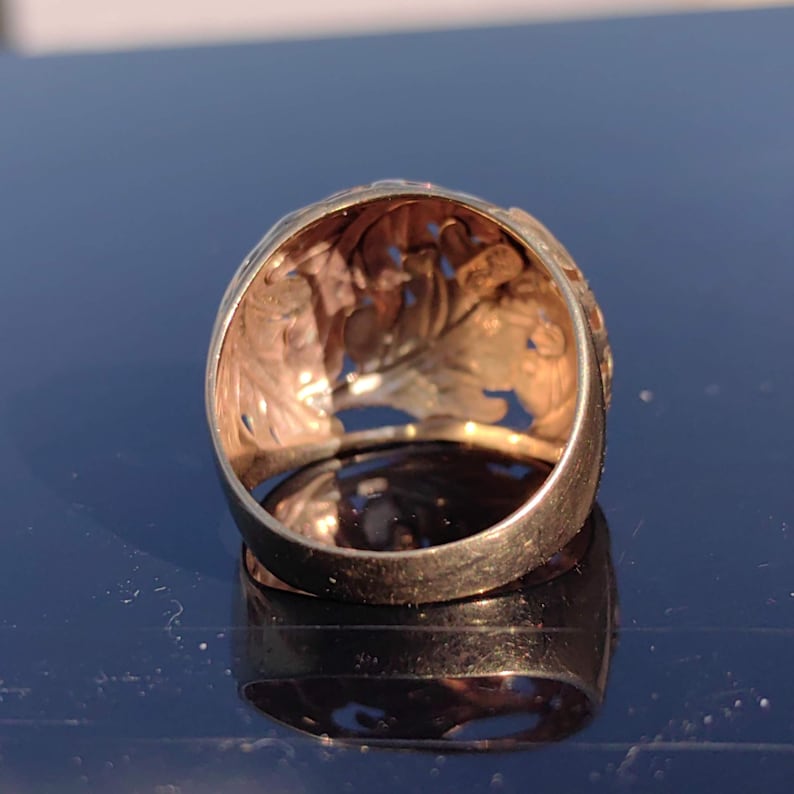 May include: A gold ring with a detailed, intricate design. The ring is made of yellow gold and has a filigree pattern.