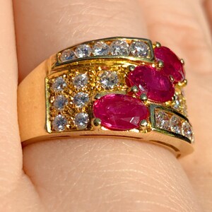 May include: A gold ring with three oval-shaped ruby gemstones and a band of pave-set diamonds.