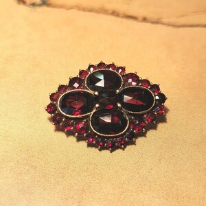 May include: A vintage brooch with a cluster of red garnet stones set in a gold tone metal frame.