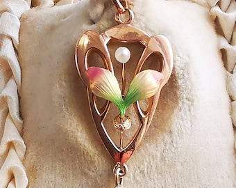 Peut inclure: Un pendentif en or avec un motif floral délicat. Le pendentif présente deux fleurs en émail rose et vert avec une perle au centre. Le pendentif est suspendu à une chaîne en or avec une perle en goutte.