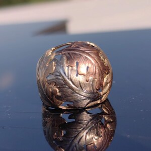May include: A silver ring with a detailed leaf design. The leaves are cut out and have a two-tone finish, with some leaves appearing gold and others silver.