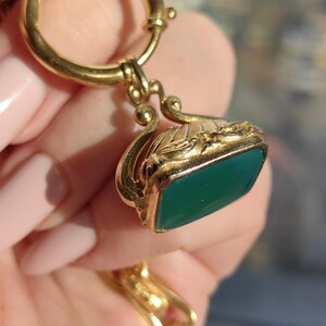 May include: A gold chain with a green stone fob. The fob has a decorative design and is attached to a ring.