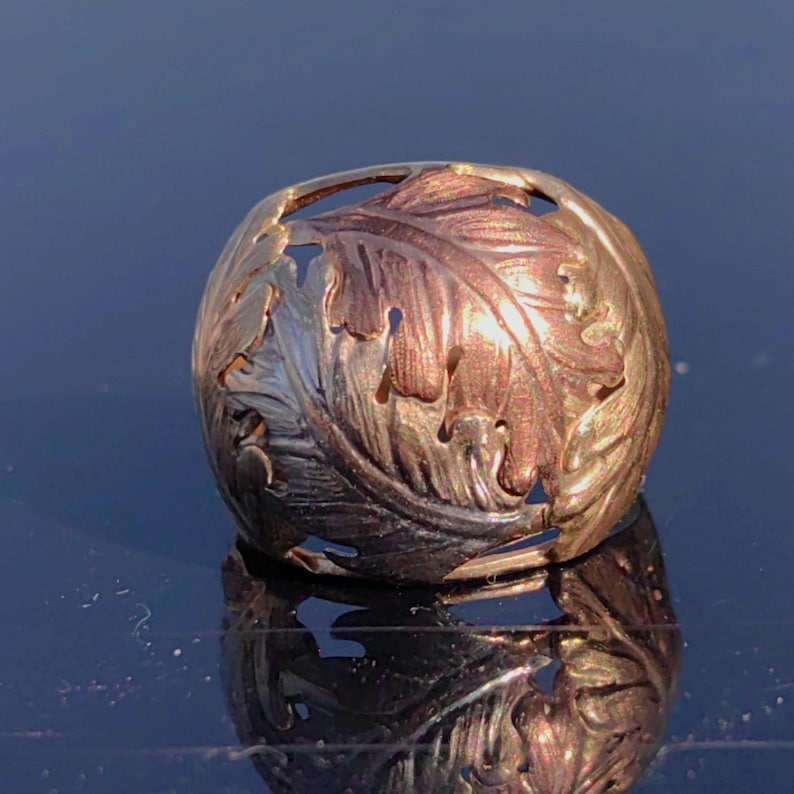 May include: A gold ring with a detailed design of leaves. The ring is made of two-toned gold, with a lighter gold color on the inside and a darker gold color on the outside.