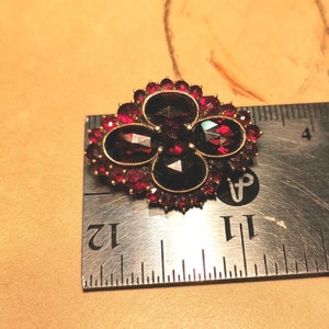 May include: A red garnet brooch with four oval-shaped stones set in a gold-toned metal frame. The brooch is surrounded by smaller red garnets. The brooch is about 1.5 inches wide.