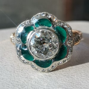 May include: A vintage engagement ring with a large round diamond surrounded by a halo of smaller diamonds. The ring is set in white gold and features a green enamel design.