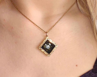 May include: A gold chain necklace with a square pendant featuring a black and white floral design. The pendant is framed with a gold border.