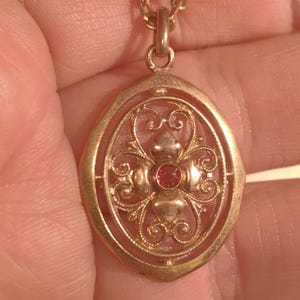 May include: A gold pendant necklace with a filigree design and a red gemstone in the center.