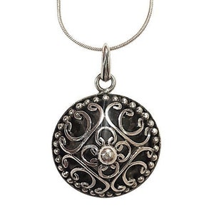 May include: A silver pendant necklace with a round, filigree design. The pendant features a delicate floral pattern with a small, clear stone in the center.